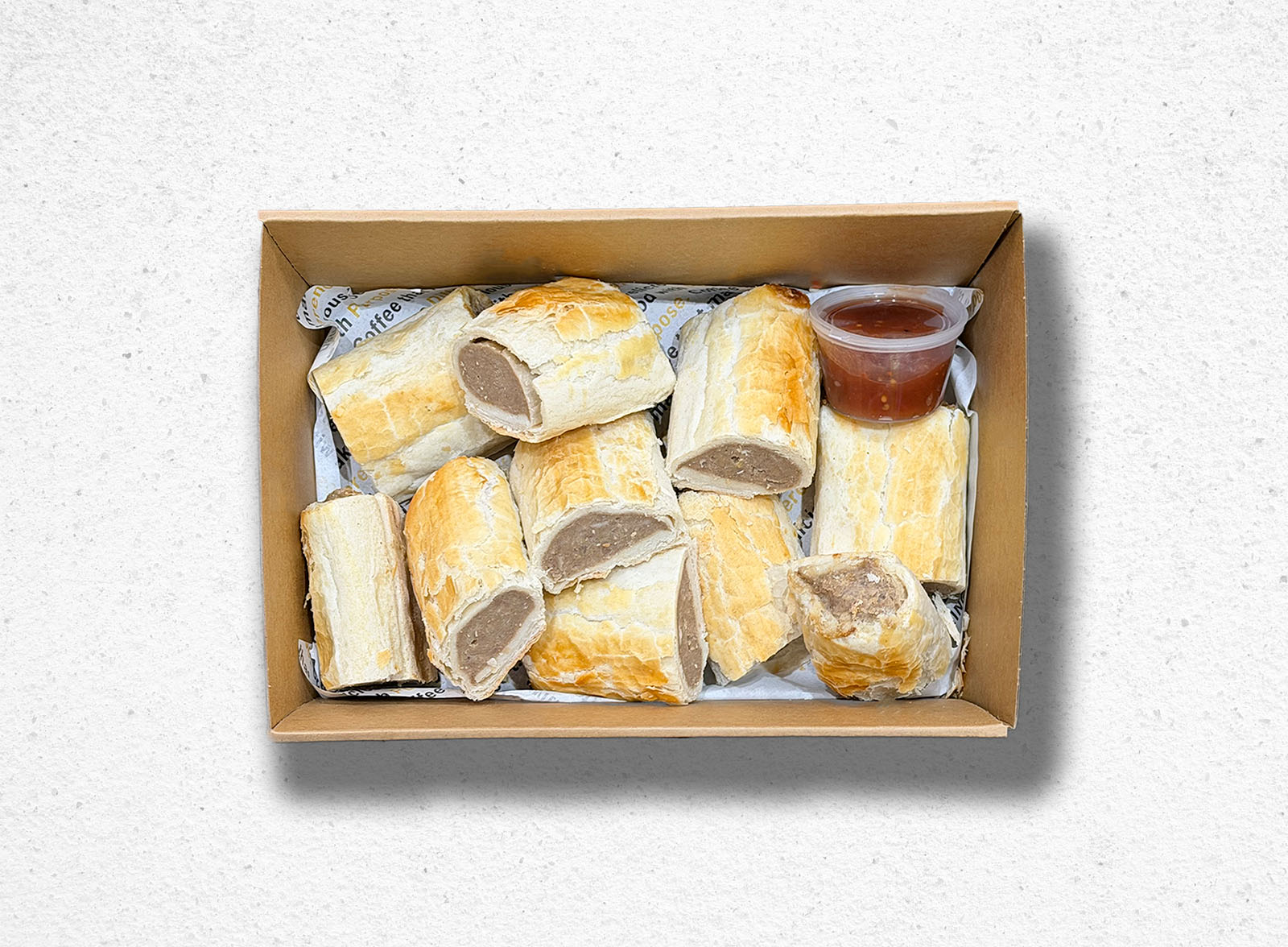 Box of sausage rolls with a side of sauce on a light gray background